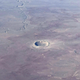 A bowl-shaped crater at center is the main detail on the otherwise flat, red-grey Arizona terrain.
